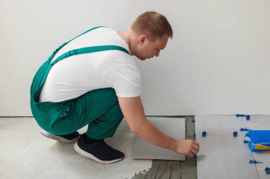 Worker installing ceramic tile on floor near wall