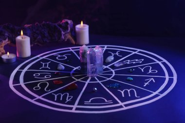 Zodyak işaretleri için doğal taşlar, astroloji çizelgesi ve koyu mavi masada yanan mumlar. Renk tonu etkisi