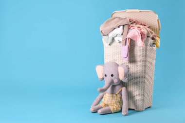 Laundry basket with baby clothes and soft toy on light blue background. Space for text