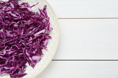 Plate with shredded fresh red cabbage on white wooden table, top view. Space for text