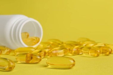 Open medicine bottle with scattered pills on yellow background, closeup