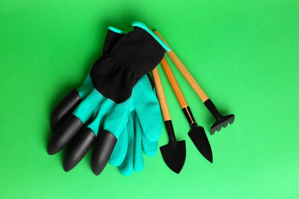 Gardening gloves and tools on green background, flat lay