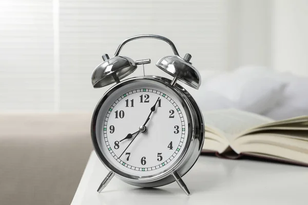 Silver alarm clock on white nightstand in bedroom