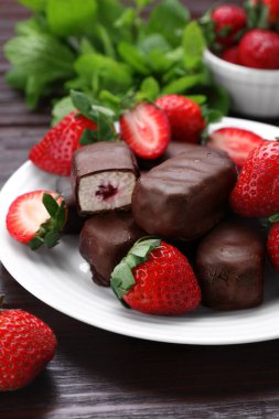 Delicious glazed curd snacks, mint leaves and fresh strawberries on wooden table, closeup