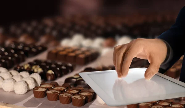 Production line of chocolate candies. Man working with tablet, closeup