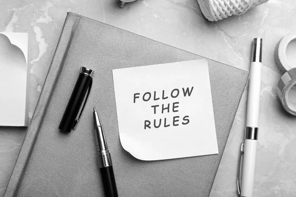 Paper note with phrase Follow The Rules and stationery on grey marble table, flat lay
