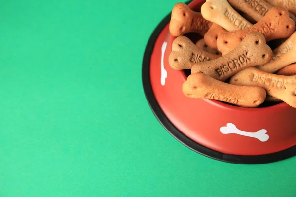 Bone shaped dog cookies in feeding bowl on green background, space for text