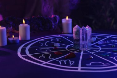 Zodyak işaretleri için doğal taşlar, astroloji çizelgesi ve koyu mavi masada yanan mumlar. Renk tonu etkisi