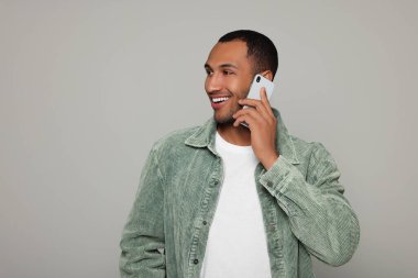 Smiling African American man talking on smartphone against light grey background. Space for text
