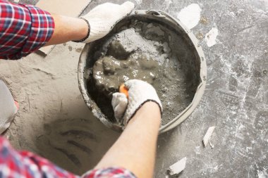 Worker with trowel mixing cement in bucket indoors, closeup