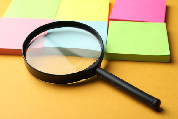 Увеличитель стекла и различные наклейки памяти на оранжевом фоне, крупным планом. Поиск концепции ключевых слов