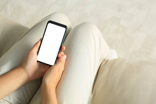 Young woman with smartphone on sofa indoors, closeup