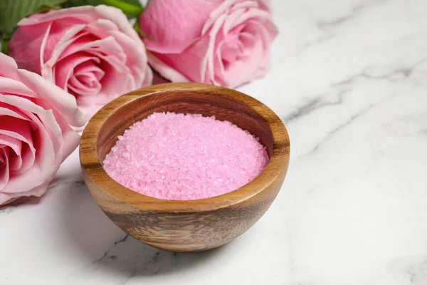 Wooden bowl with pink sea salt and beautiful roses on white marble table