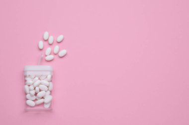 Tasty dragee candies and container on pink background, flat lay. Space for text