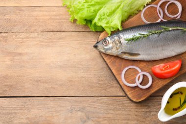 Board with delicious salted herring and ingredients on wooden table, flat lay. Space for text