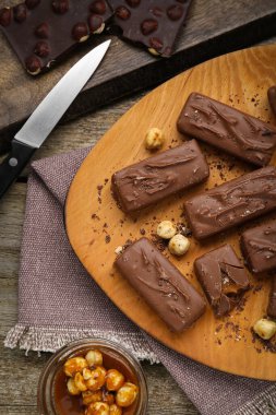 Delicious chocolate candy bars with caramel and nuts on wooden table, flat lay