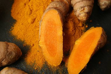 Turmeric roots and powder on black textured table, closeup
