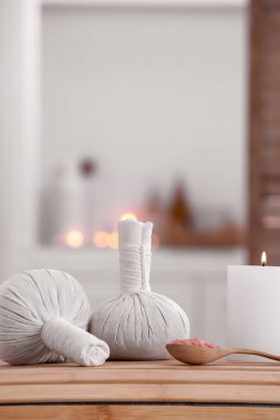 Spa composition with burning candle and herbal bags on massage table in wellness center, space for text