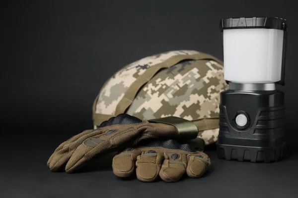 Tactical gloves, helmet and camping lantern on black background. Military training equipment