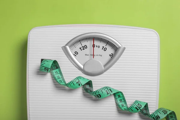 Weight loss concept. Scales and measuring tape on green background, top view