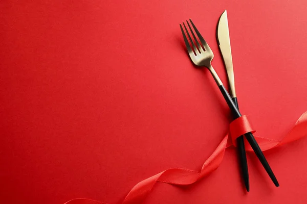 Cutlery set and ribbon on red background, flat lay with space for text. Romantic table setting