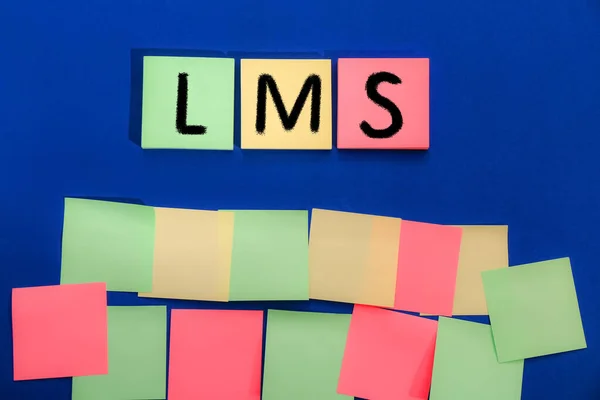 Learning management system. Colorful sticky notes with abbreviation LMS on blue background, top view