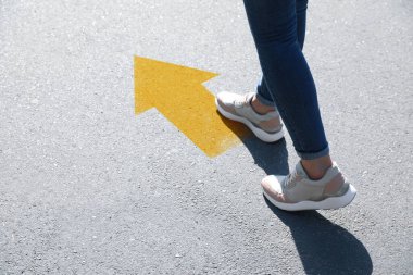 Planning future. Woman walking to drawn mark on road, closeup. Yellow arrow showing direction of way clipart