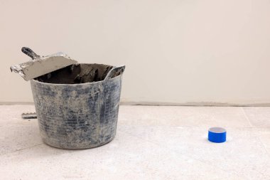 Bucket of adhesive mix and spatula on floor indoors, space for text. Tiles installation process