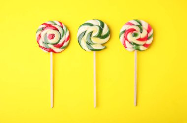 Colorful lollipops on yellow background, flat lay