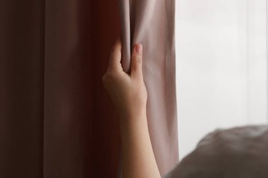 Woman opening stylish curtains at home, closeup