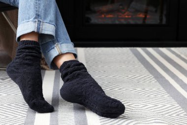 Woman in warm socks relaxing near fireplace at home, closeup