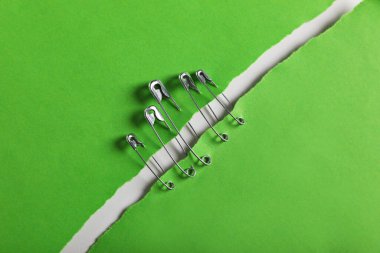 Pieces of green paper sheets joined with safety pins on white background, top view