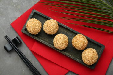 Delicious sesame balls, green leaf and chopsticks on grey table, flat lay