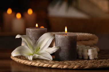Spa composition with burning candles, lily flower and towels on wooden table in wellness center