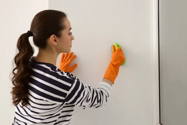 Woman in rubber gloves cleaning wall with brush indoors