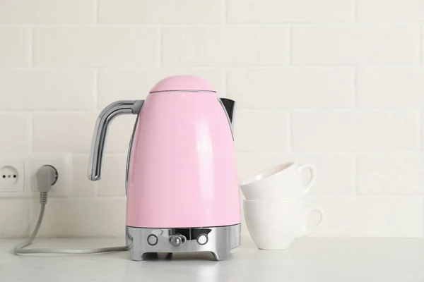 Modern electric kettle and cups on counter in kitchen
