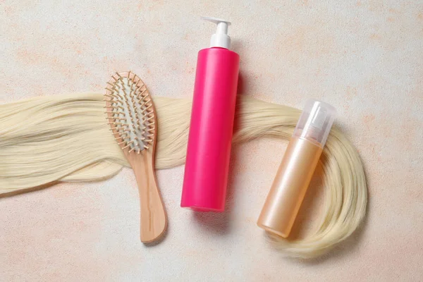 Spray bottles with thermal protection, lock of blonde hair and hairbrush on beige textured table, flat lay