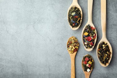 Açık gri masada, tahta kaşıklarda farklı türde kuru bitkisel çay. Metin için boşluk