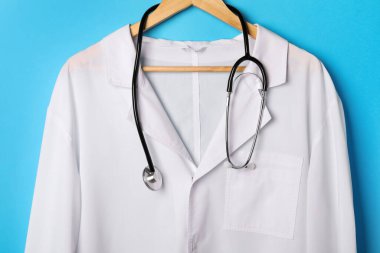 Medical uniform and stethoscope on light blue background