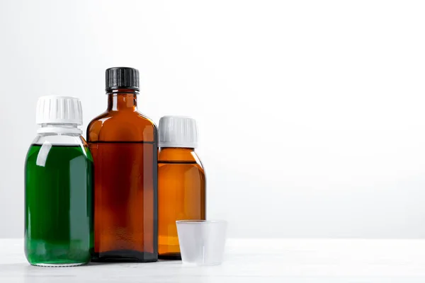 Bottles of syrups with measuring cup on wooden table against white background, space for text. Cough and cold medicine