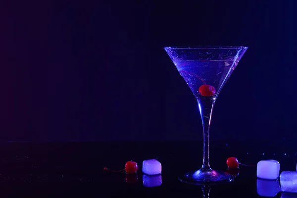 Fresh martini near ice and cherries on mirror table in neon lights, space for text