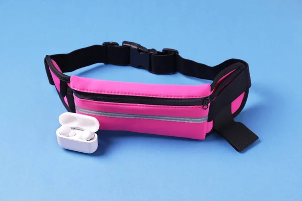 Stylish pink waist bag and earphones on light blue background