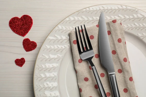 Plate with cutlery and decorative hearts on white wooden table for romantic dinner, top view