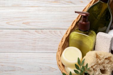 Shampoo bottles, loofah, pumice and solid shampoo bars in wicker basket on white wooden table, top view. Space for text