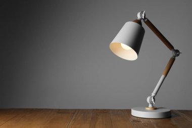 Stylish modern desk lamp on wooden table against grey background, space for text
