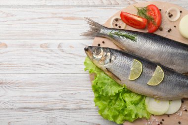 Board with delicious salted herrings and ingredients on white wooden table, top view. Space for text