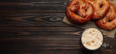 Tasty freshly baked pretzels and mug of beer on wooden table, flat lay with space for text. Banner design