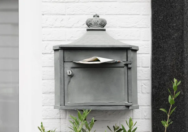 Metal letter box with newspaper on white brick wall outdoors