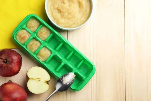 Apple puree in ice cube tray ready for freezing with fresh apple fruits on wooden table, flat lay. Space for text