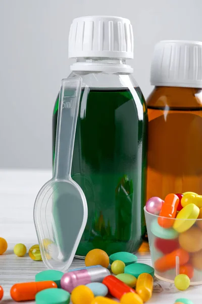Bottles of syrups with pills on wooden table against white background, closeup. Cough and cold medicine